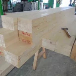 Przygotowane elementy konstrukcyjne z drewna klejonego warstwowo, ułożone na kozłach, z widocznym młotkiem na jednym z belek.