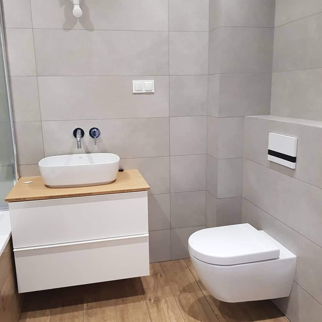 Nowoczesna łazienka z umywalką nablatową na szafce z drewnianym blatem, podwieszaną toaletą i szarymi płytkami.