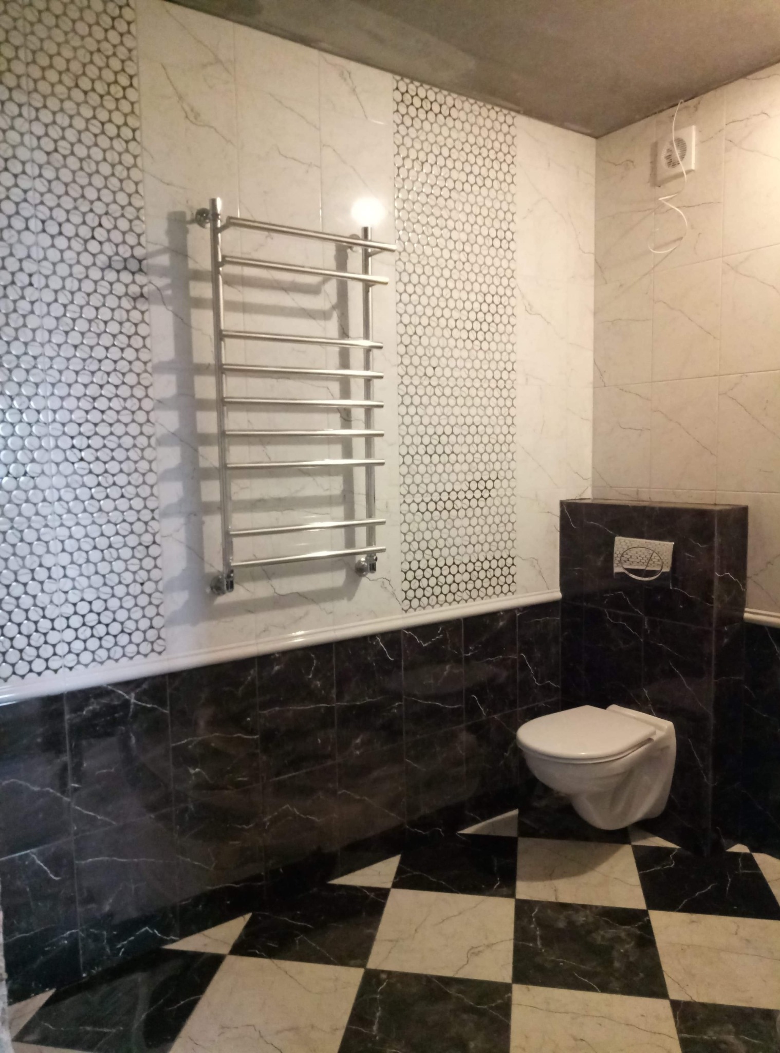 Wykończona łazienka z czarno-białą szachownicą na podłodze, mozaiką na ścianie oraz grzejnikiem drabinkowym.