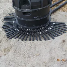 Czarny kolektor gruntowy z rurami ułożonymi promieniście w piasku, widoczny numer seryjny na obudowie.