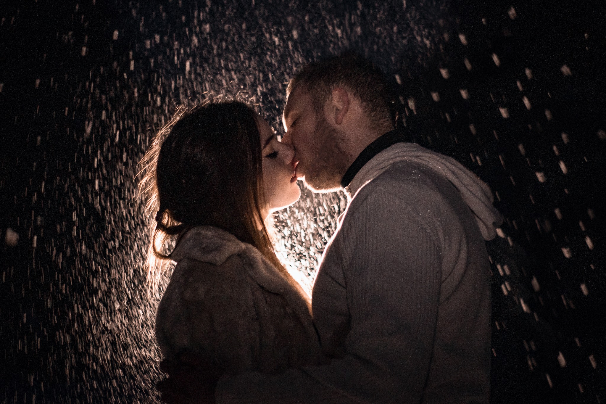 Para całująca się w strugach deszczu, podświetlona od tyłu, sylwetki w ciemnych ubraniach.