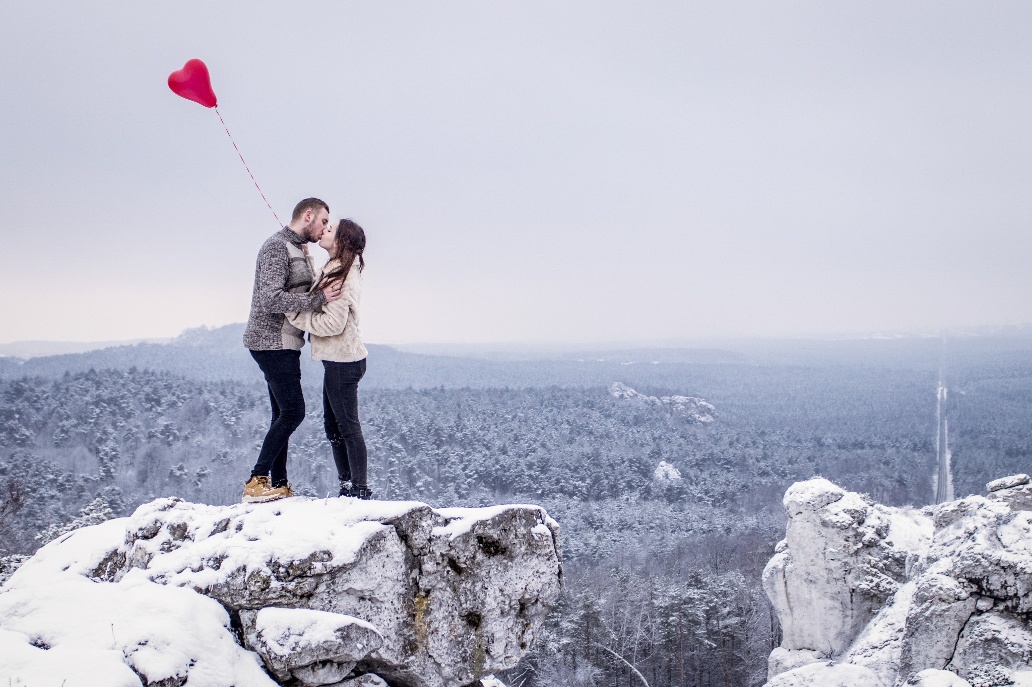 Para całująca się na ośnieżonym klifie z czerwonym balonem w kształcie serca, zimowy krajobraz w tle.
