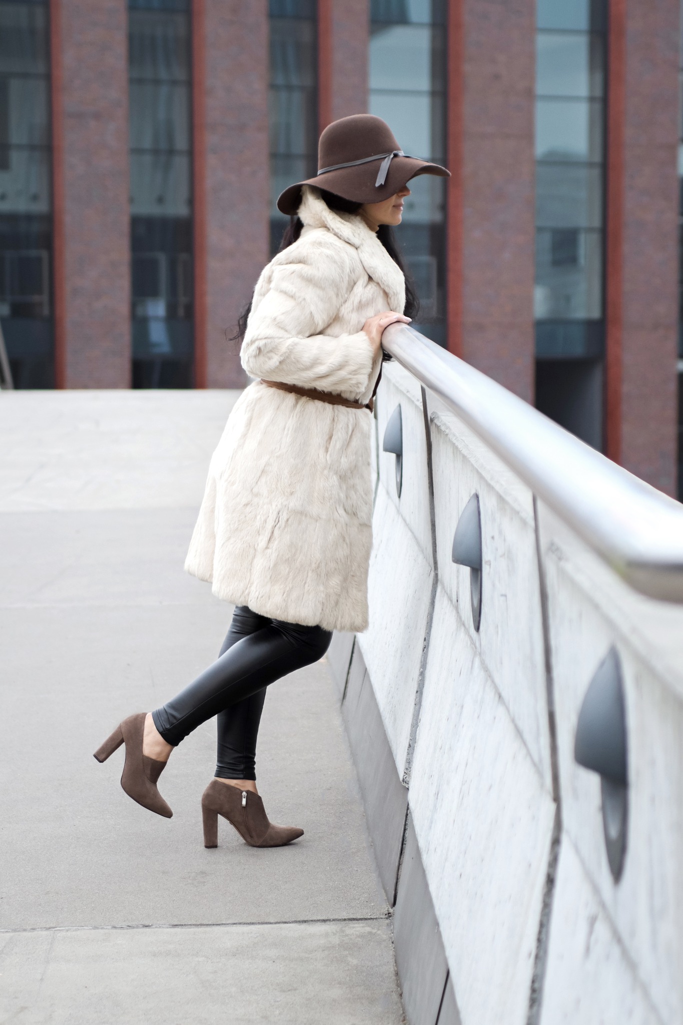 Kobieta w futrze, kapeluszu i botkach na obcasie, oparta o barierkę w Żarkach, spogląda w dal.