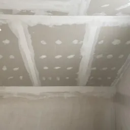 Montaż płyt kartonowo-gipsowych na suficie poddasza, widoczne łączenia i wkręty przed szpachlowaniem, surowy stan wykończenia wnętrza.