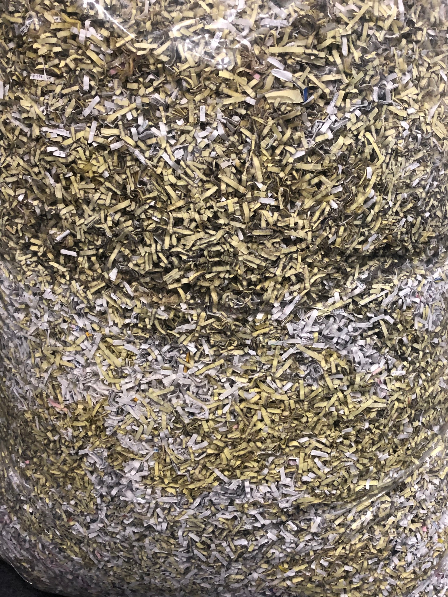 Worek wypełniony pociętymi na drobne paski dokumentami w odcieniach bieli i beżu, widoczne fragmenty tekstu na niektórych paskach.