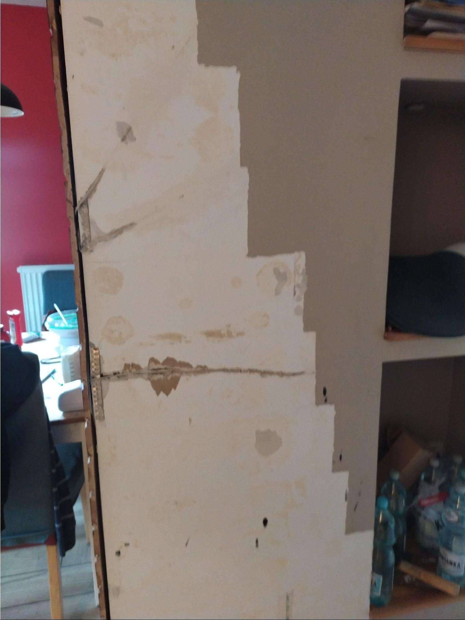 Fragment ściany w trakcie przygotowania do malowania: widoczne ślady po usuniętej tapecie, nierówności i częściowo nałożona warstwa farby gruntującej w kolorze beżowym.