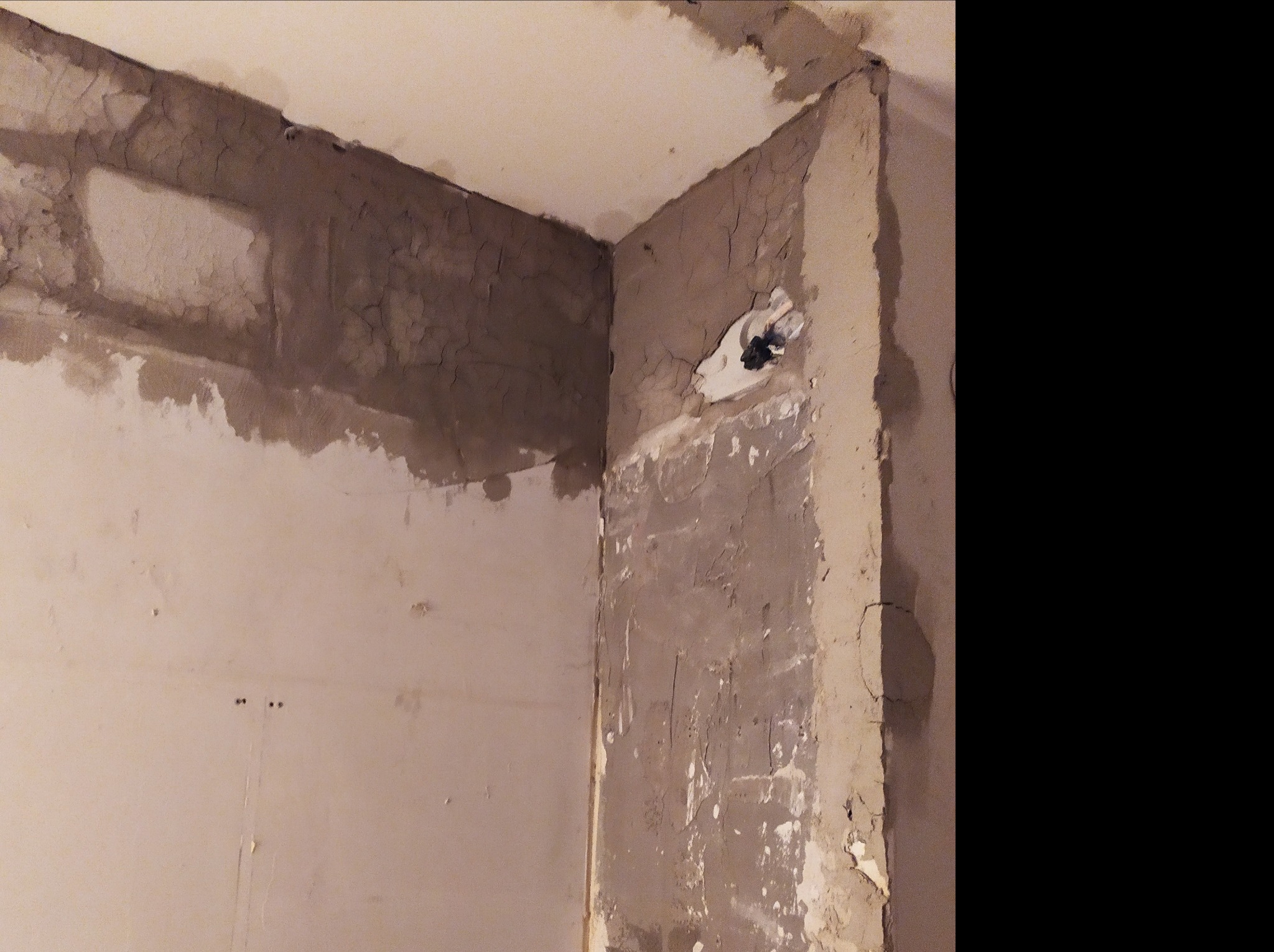 Narożnik pokoju w trakcie prac przygotowawczych do malowania: ściany pokryte warstwą szpachli, widoczne pęknięcia i niedoskonałości, odsłonięta instalacja elektryczna w puszce.