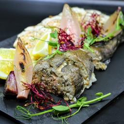 Restauracja Stare Kino - Elegancko podana, faszerowana ryba z cytryną i grillowaną cebulą na czarnym, kamiennym talerzu, udekorowana świeżymi ziołami.