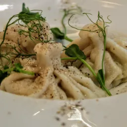 Dwa chinkali posypane pieprzem i udekorowane młodymi pędami groszku, podane na białym talerzu.