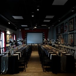 Restauracja Stare Kino - Uroczysta sala w stylu retro z długim stołem bankietowym, czarnymi obrusami z błyszczącymi bieżnikami, nakryciami, świecami i dekoracjami z piór, tłem z ekranem i ścianami ozdobionymi plakatami...