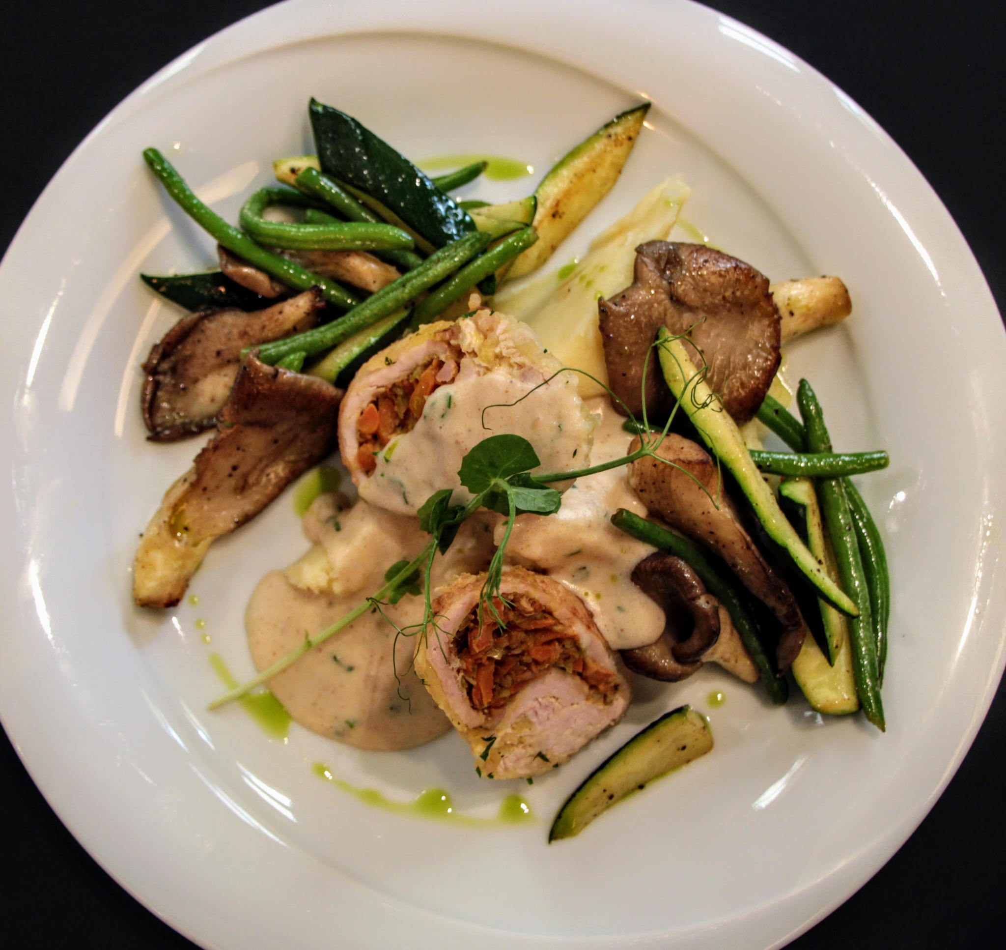 Elegancko podane roladki z kurczaka z farszem warzywnym, polane sosem, z dodatkiem grillowanych warzyw i grzybów na białym talerzu.