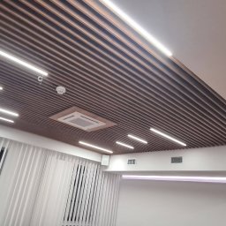 Interactive System Martin Pazdecki - Salka konferencyjna z drewnianym, lamelowym sufitem, oświetleniem LED i klimatyzacją, widziana pod kątem.