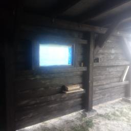 Usługi Wielobranżowe Agata Opioła - Drewniana wiata z oknem zabezpieczonym folią, widoczne półki z deskami i betonowa podstawa słupa.