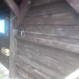 Usługi Wielobranżowe Agata Opioła - Wnętrze wiaty drewnianej z widoczną konstrukcją dachu, deskami obiciowymi i półką z książkami w rogu.