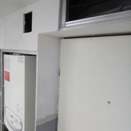 Usługi Wielobranżowe Agata Opioła - Fragment zabudowy z płyt gipsowo-kartonowych w Strzelinie, widoczny piec gazowy, szpachlowane ściany i fragment sufitu z metalową konstrukcją.