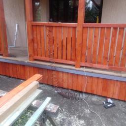 Usługi Wielobranżowe Agata Opioła - Montaż drewnianego tarasu: widok na fragment konstrukcji z pomalowanymi deskami, widoczny kompresor i zszywacz pneumatyczny, deski na kozłach w tle.