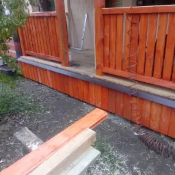 Budowa tarasu: pomalowane deski i podbitka w trakcie montażu, widoczny poziomica i zwinięty przewód pneumatyczny.