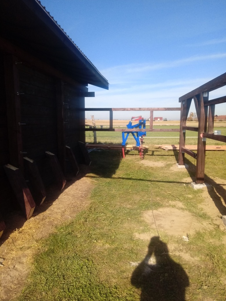 Budowa wiaty drewnianej z widoczną konstrukcją szkieletową i częściowo zamontowanymi deskami, narzędzia budowlane w tle, widok z zewnątrz w słoneczny dzień.