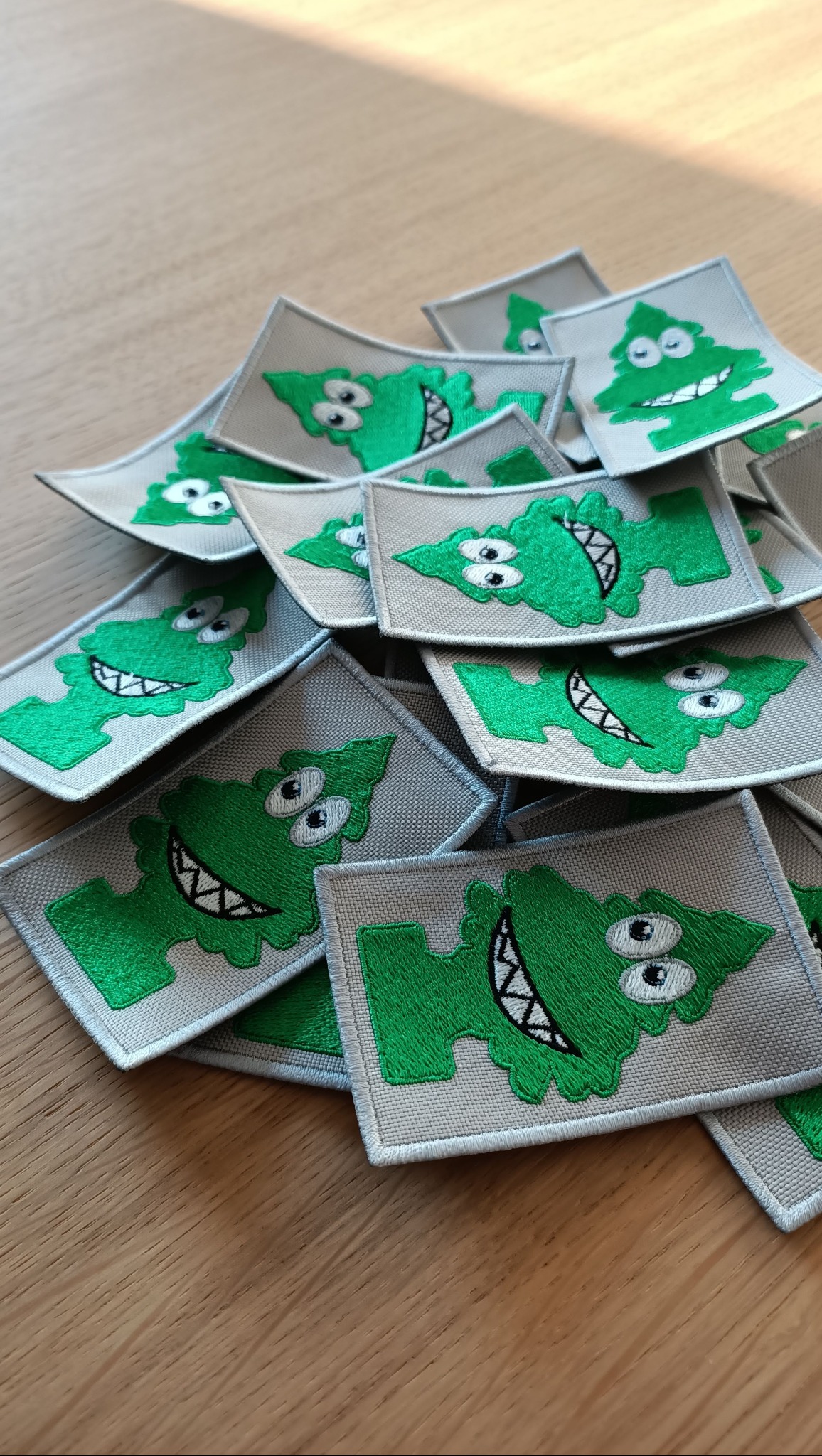 Stos szarych naszywek z zielonym, kreskówkowym potworem z zębami na drewnianym blacie.