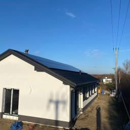 Elektroserwis Arkadiusz Miszczuk - Montaż paneli słonecznych na dachu domu jednorodzinnego w Kobyłce, widoczne panele w czarnej ramie i pracownik na dachu, błękitne niebo w tle.