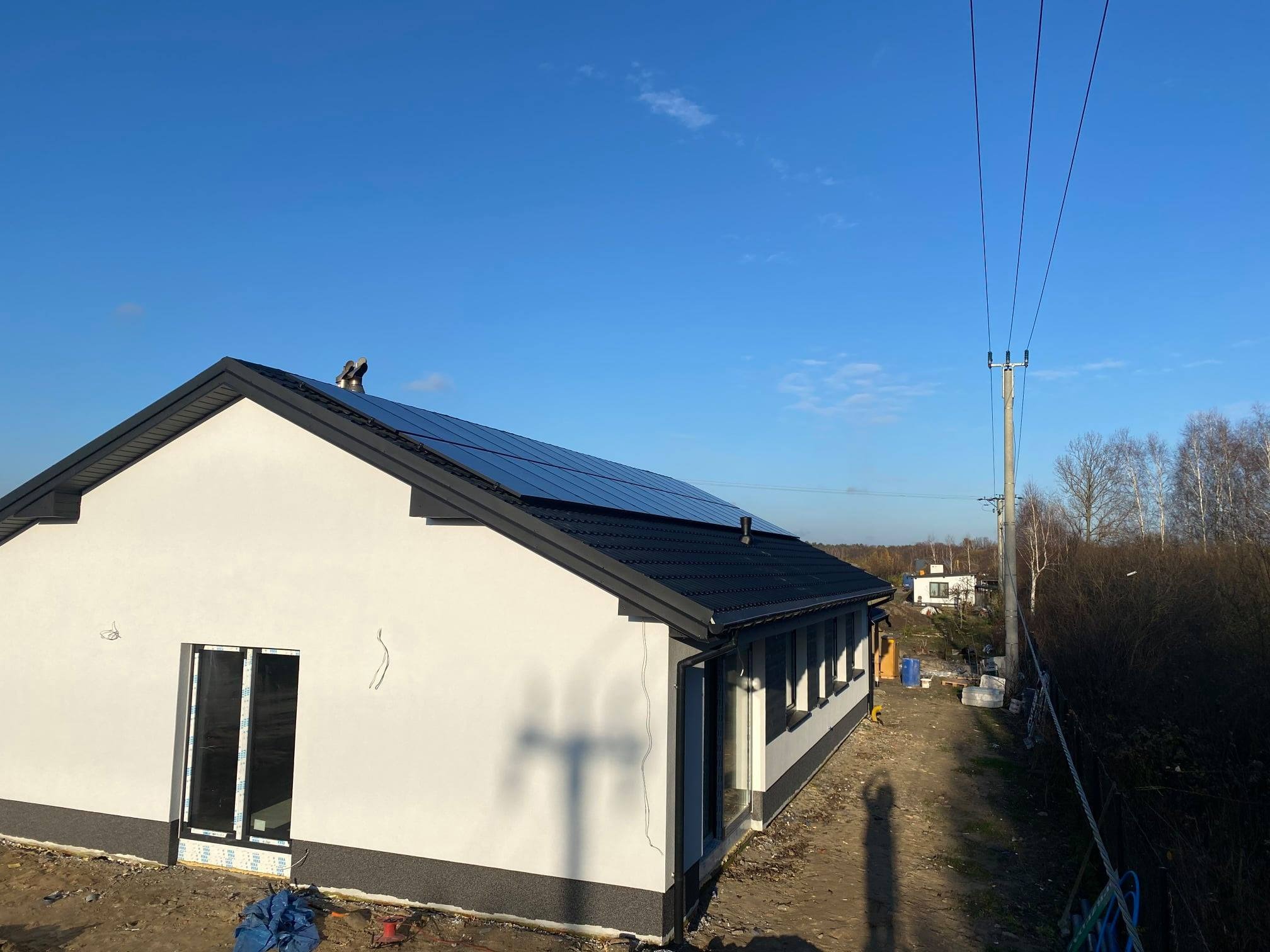 Montaż paneli słonecznych na dachu domu jednorodzinnego w Kobyłce, widoczne panele w czarnej ramie i pracownik na dachu, błękitne niebo w tle.