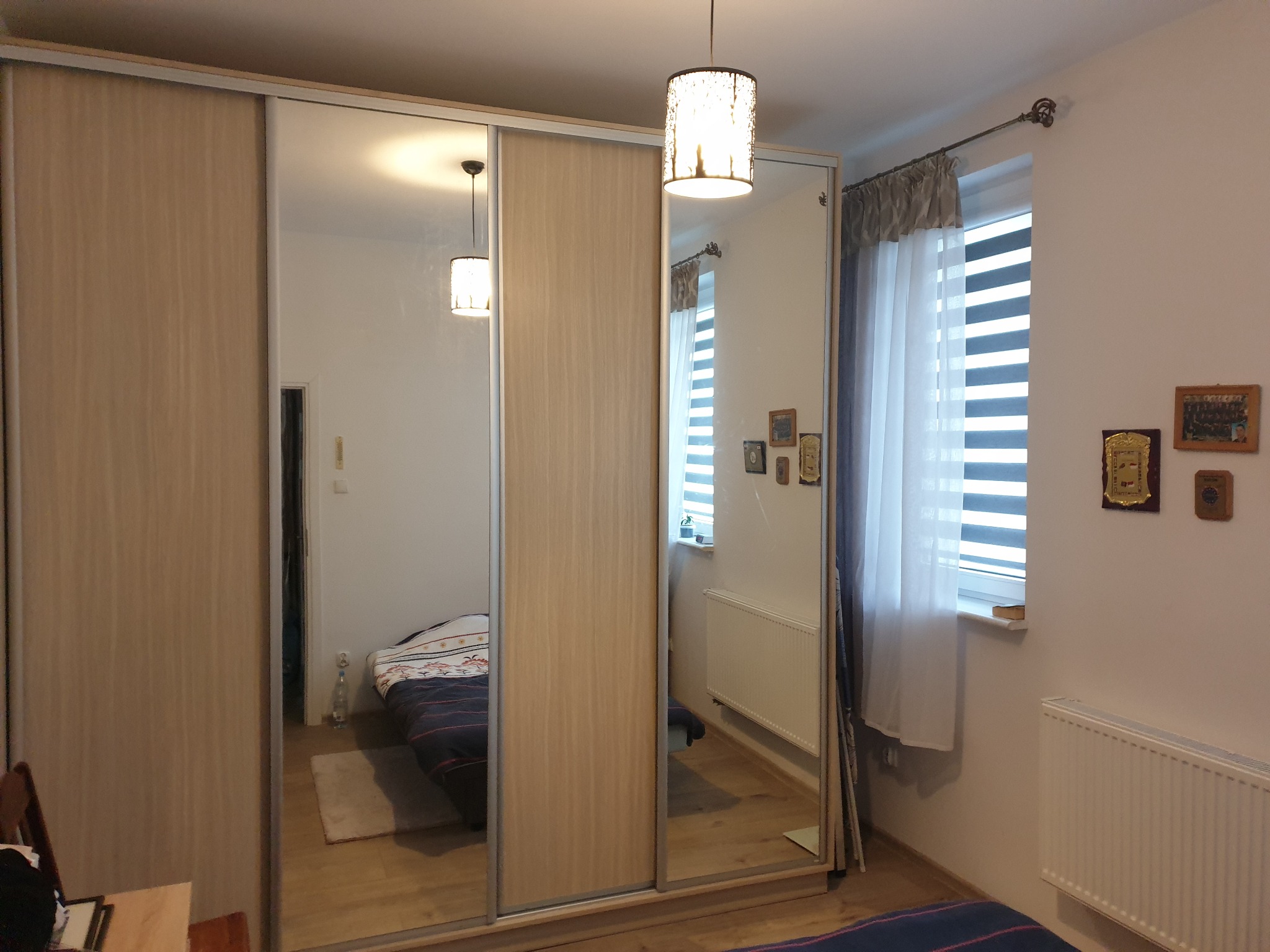 Szafa przesuwna z lustrami w sypialni, odbicie łóżka i okna z żaluzjami dzień-noc.