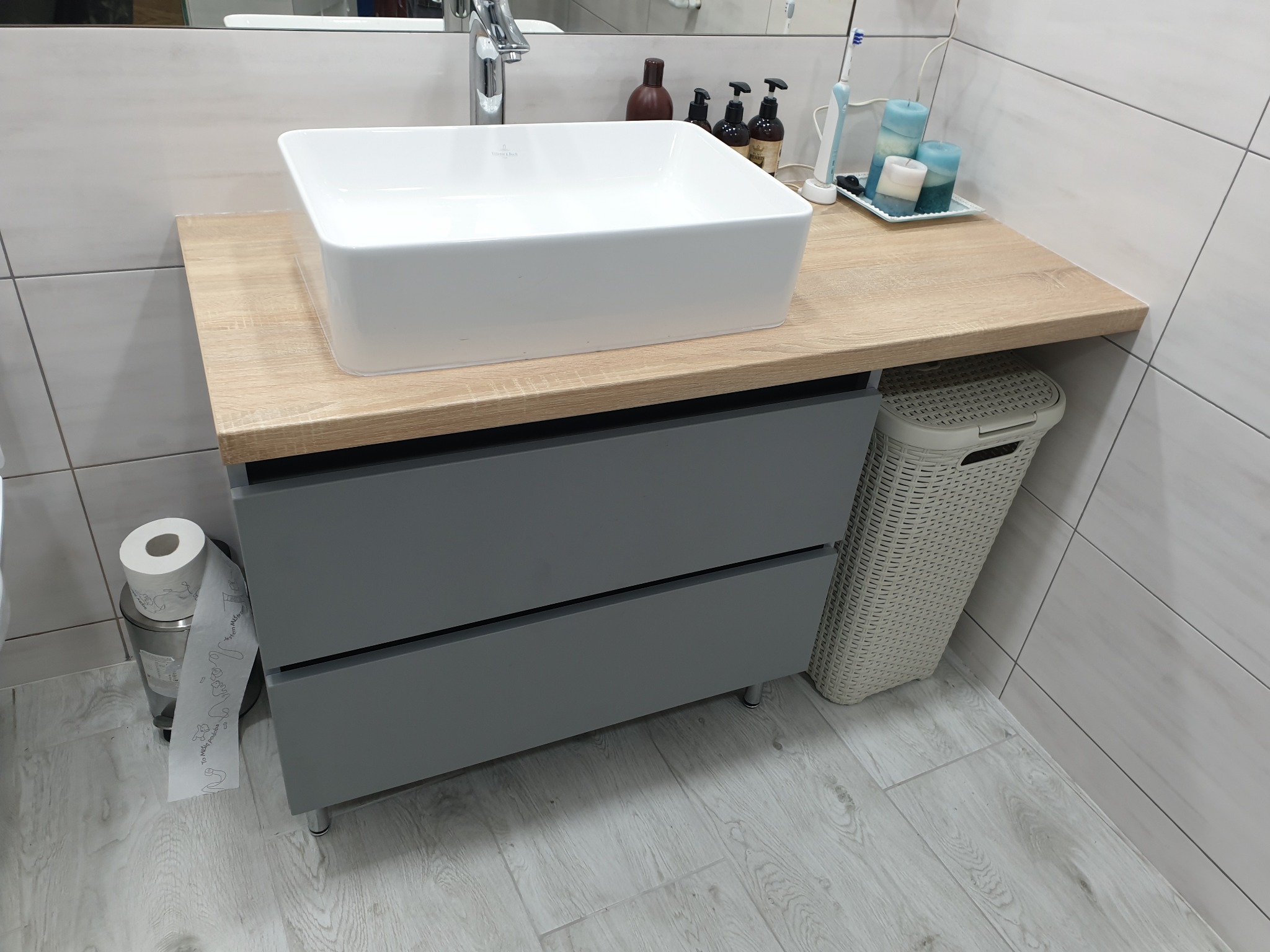 Szara szafka łazienkowa z dwiema szufladami, drewnianym blatem i nablatową, prostokątną umywalką Villeroy & Boch.