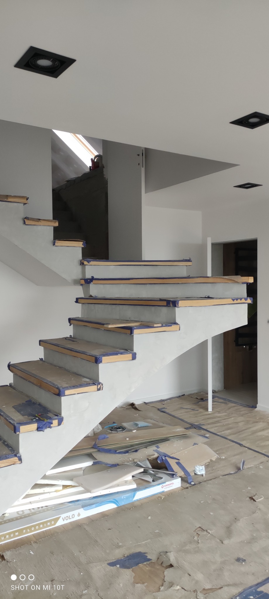 Schody betonowe w trakcie wykończenia, zabezpieczone niebieską taśmą malarską, widoczne przygotowane stopnie i bałagan na podłodze.