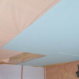 Płyta gipsowa na suficie, częściowo zakryta folią. Widoczne drewniane elementy konstrukcyjne i fragment ściany. Prace wykończeniowe w trakcie realizacji.