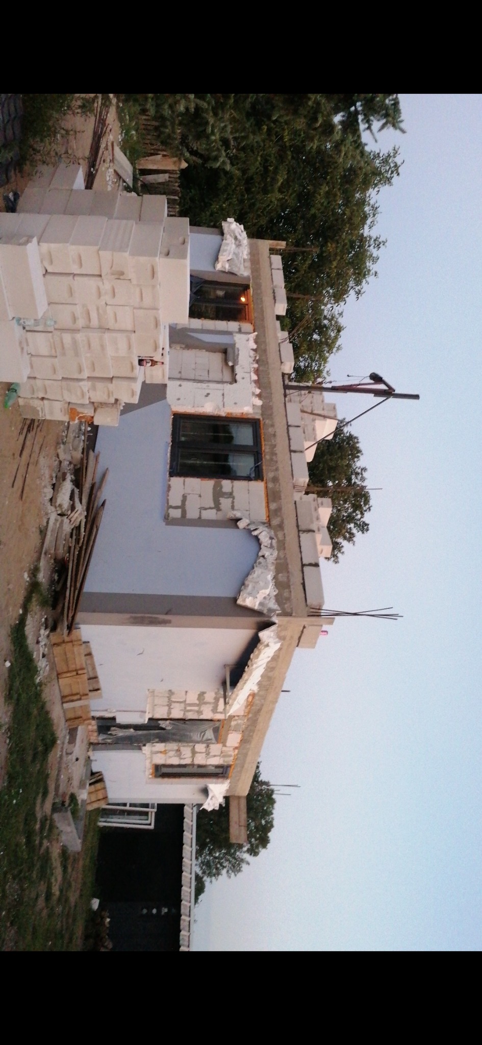 Wznoszenie ścian zewnętrznych budynku z bloczków betonu komórkowego, widoczne okno z czarną ramą i fragment niebieskiego tynku.