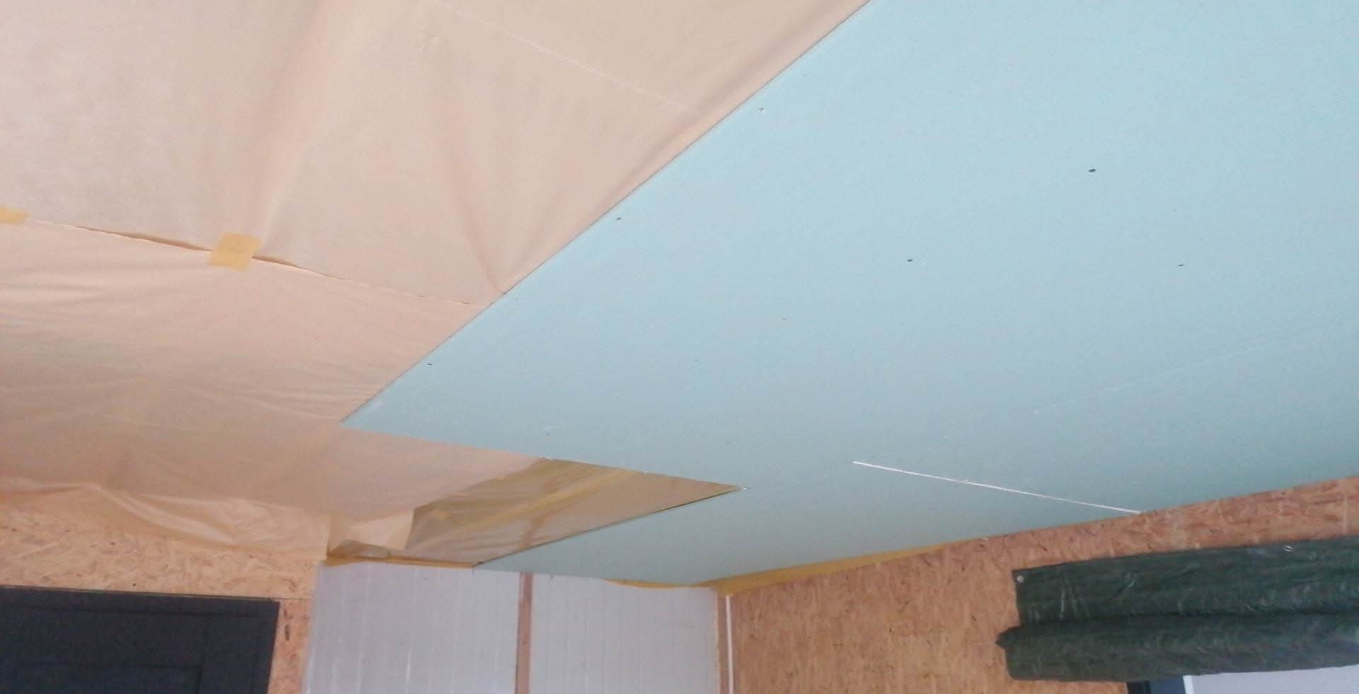 Płyta gipsowa na suficie, częściowo zakryta folią. Widoczne drewniane elementy konstrukcyjne i fragment ściany. Prace wykończeniowe w trakcie realizacji.