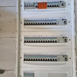 Rozdzielnica elektryczna z licznymi bezpiecznikami i wyłącznikami różnicowoprądowymi marki Tracon zamontowana na ścianie z surowego betonu komórkowego.