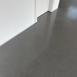 Szara, błyszcząca posadzka w pomieszczeniu z białymi ścianami i futryną drzwiową, widoczna z bliskiej perspektywy.
