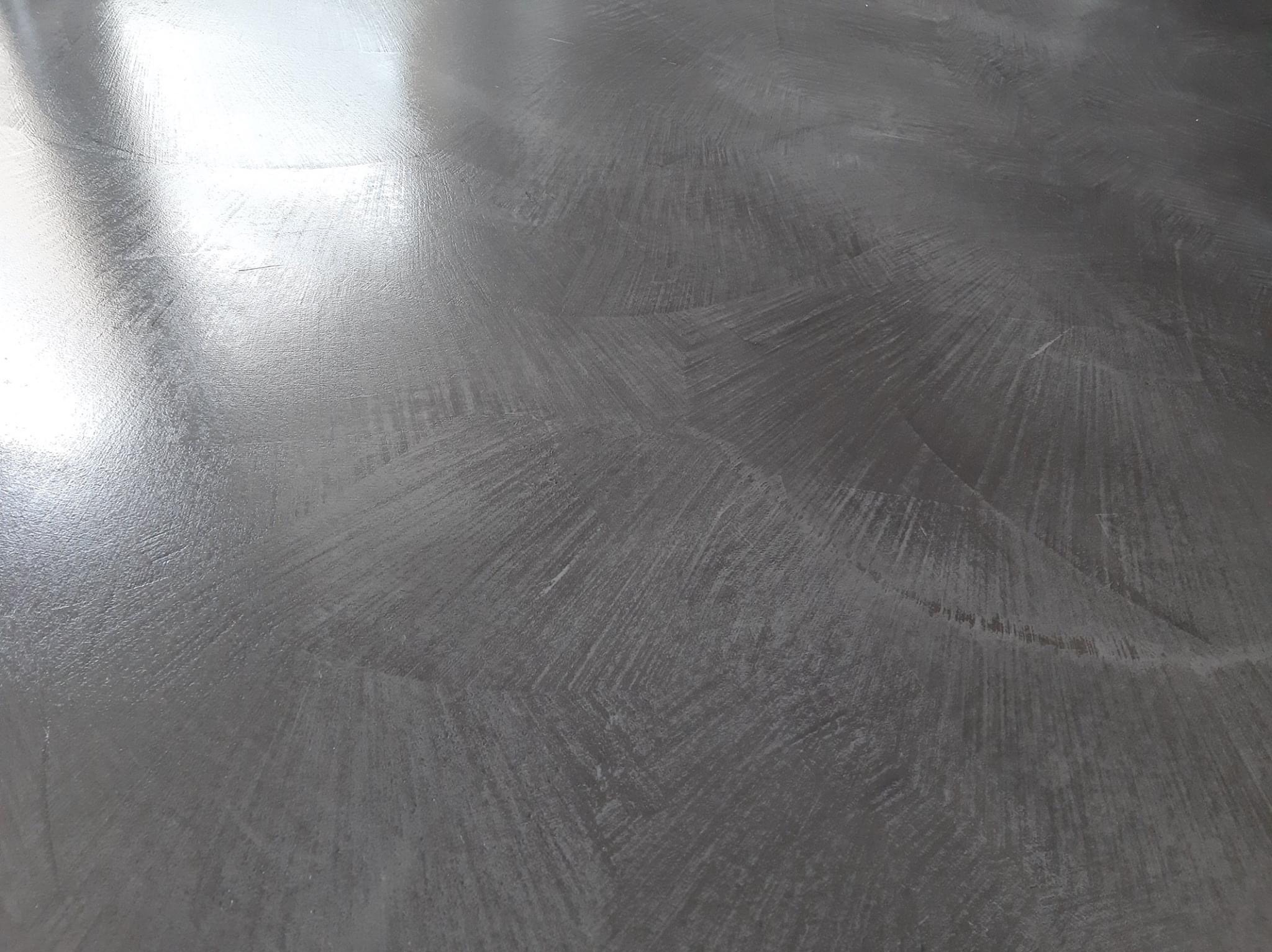 Szara, błyszcząca powierzchnia z delikatnym wzorem przypominającym promienie rozchodzące się od środka, tworzące efekt wizualny przypominający kamień polerowany.