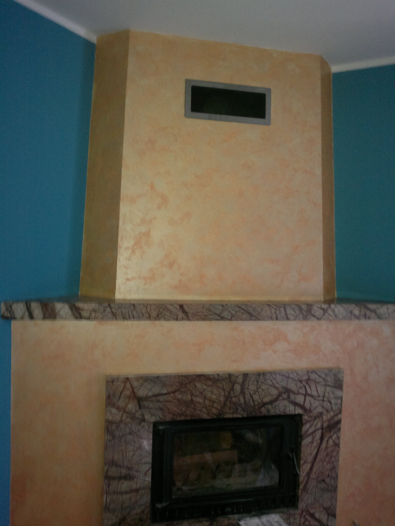 Otynkowany kominek z marmurowym obramowaniem paleniska i półką, ściana pomalowana na niebiesko.