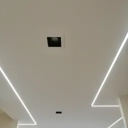 Biały sufit z wbudowanymi liniowymi lampami LED, centralnie umieszczony kwadratowy otwór na oświetlenie punktowe, widoczne ślady szpachlowania na ścianach.