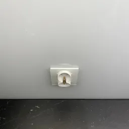 Biała, okrągła oprawa oświetleniowa sufitowa, widoczna od dołu, zamontowana na gładkim, białym suficie, z fragmentem czarnego blatu poniżej.