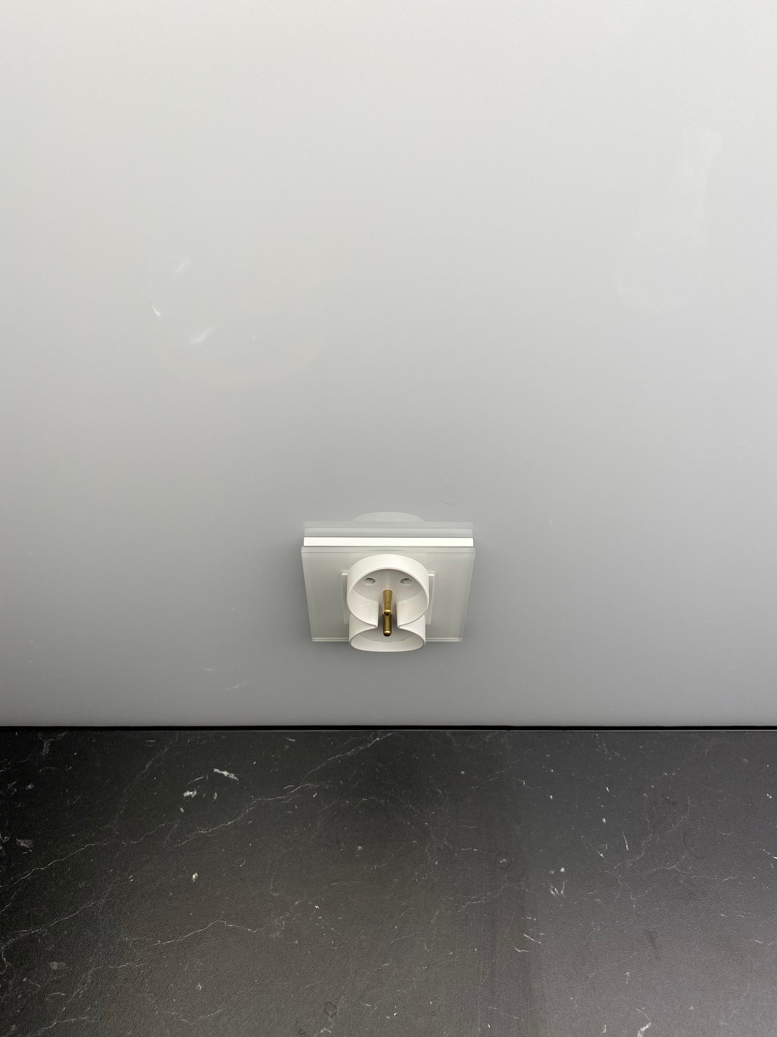 Biała, okrągła oprawa oświetleniowa sufitowa, widoczna od dołu, zamontowana na gładkim, białym suficie, z fragmentem czarnego blatu poniżej.