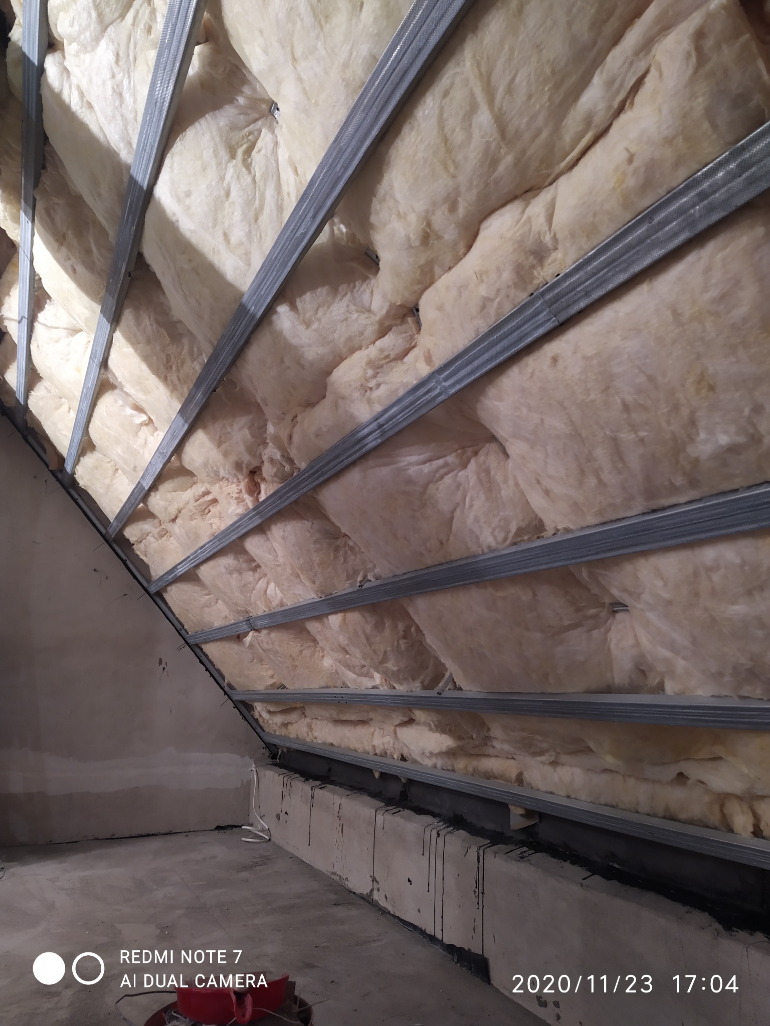 Poddasze w trakcie ocieplania wełną mineralną, widoczne metalowe profile konstrukcyjne i fragment surowego wnętrza