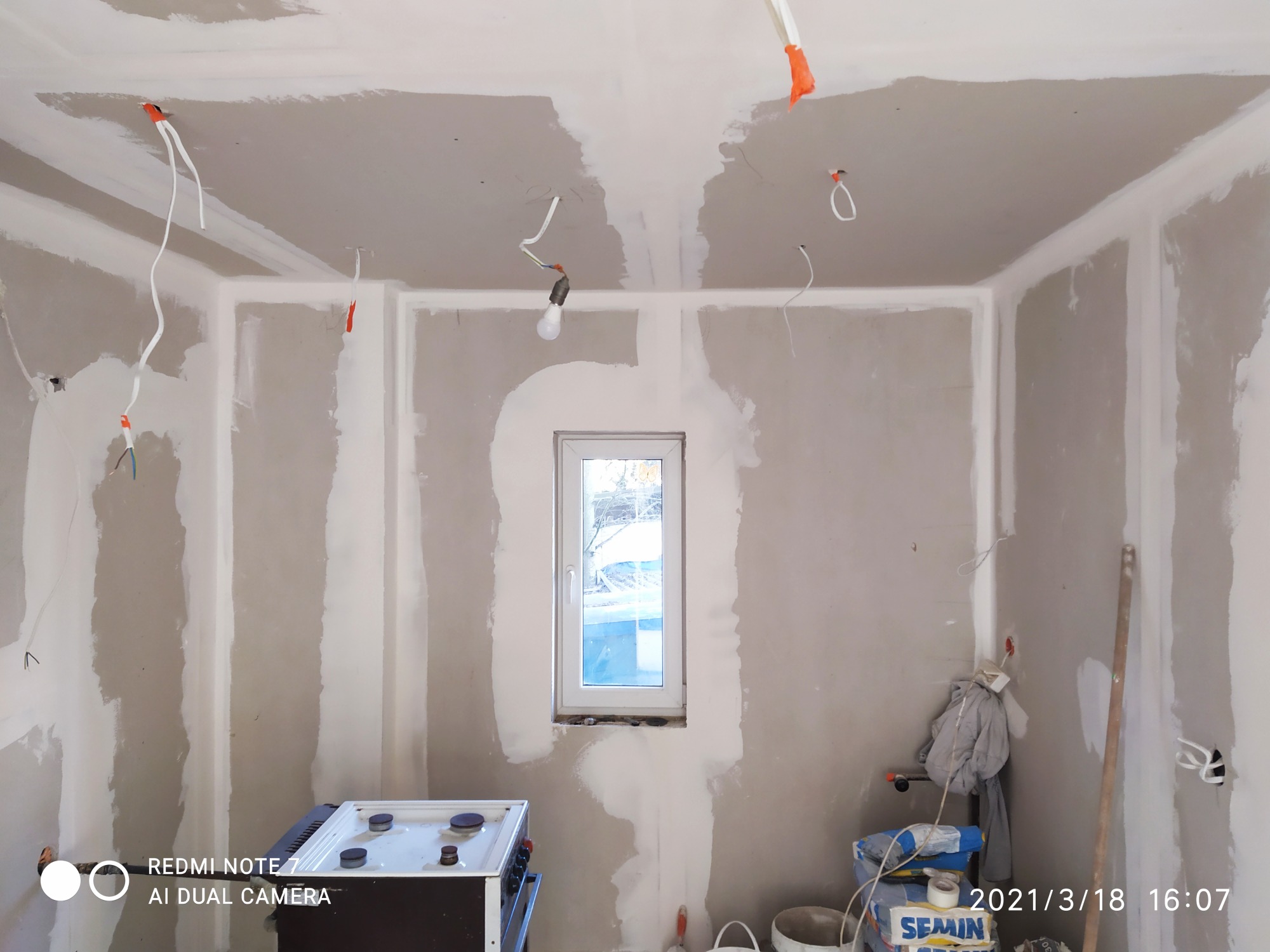 Wnętrze w trakcie prac wykończeniowych: ściany z płyt kartonowo-gipsowych z widocznymi łączeniami, częściowo pokryte warstwą gładzi, wystające przewody elektryczne, widoczny sprzęt budowlany...