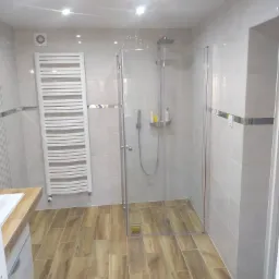 Wykończona łazienka z kabiną prysznicową typu walk-in, grzejnikiem drabinkowym i płytkami imitującymi drewno na podłodze.