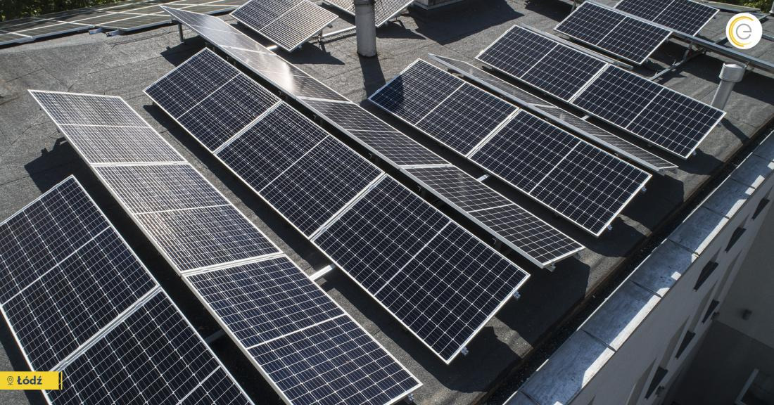 Rząd paneli fotowoltaicznych na płaskim dachu budynku, widok z góry, z widocznymi kominami wentylacyjnymi.