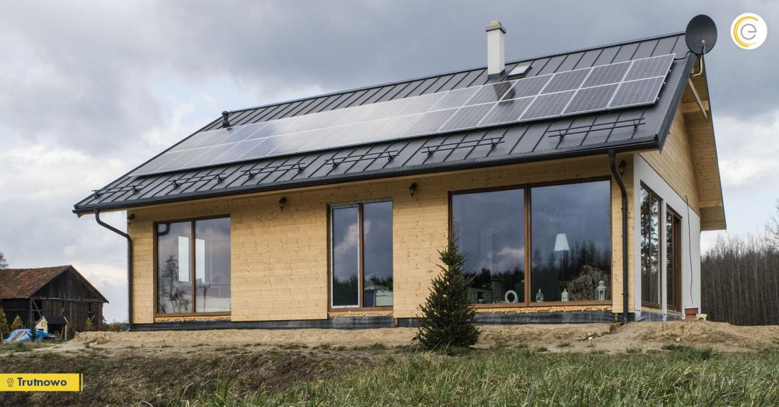 Nowoczesny dom jednorodzinny z drewnianą elewacją i panelami słonecznymi na metalowym dachu, widok z zewnątrz w pochmurny dzień.