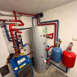 Lubas Serwis - Kotłownia z piecem Zębiec 16kW, zbiornikiem Joule i instalacją z rur w kolorach czerwonym i niebieskim. Widoczne manometry i filtry. Kotłownia w piwnicy.