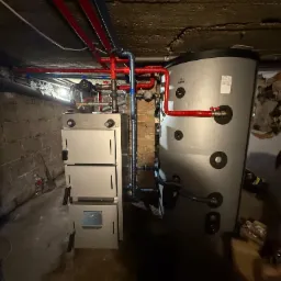 Nowoczesny piec CO z zasobnikiem w piwnicy, instalacja z rur miedzianych i plastikowych, widok na ceglany mur i betonowy sufit. CEFF, Galmet.