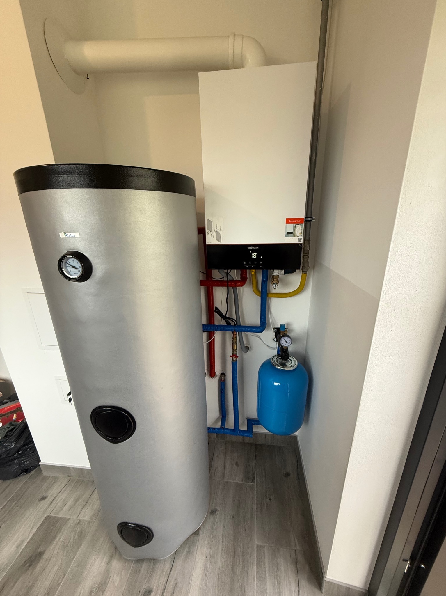 Nowoczesna instalacja grzewcza: biały piec gazowy Viessmann, srebrny zasobnik wody i niebieskie naczynie przeponowe w jasnym pomieszczeniu.