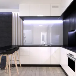 Nowoczesna kuchnia z białymi, lakierowanymi szafkami, czarnym blatem i ścianą z czarnej cegły, oświetlona listwą LED pod szafkami wiszącymi, z widocznymi dwoma drewnianymi hokerami.