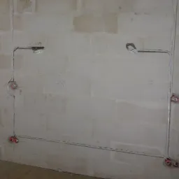 Surowa ściana z betonu komórkowego z widocznymi przewodami elektrycznymi w peszlach i puszkami instalacyjnymi, instalacja w trakcie montażu.