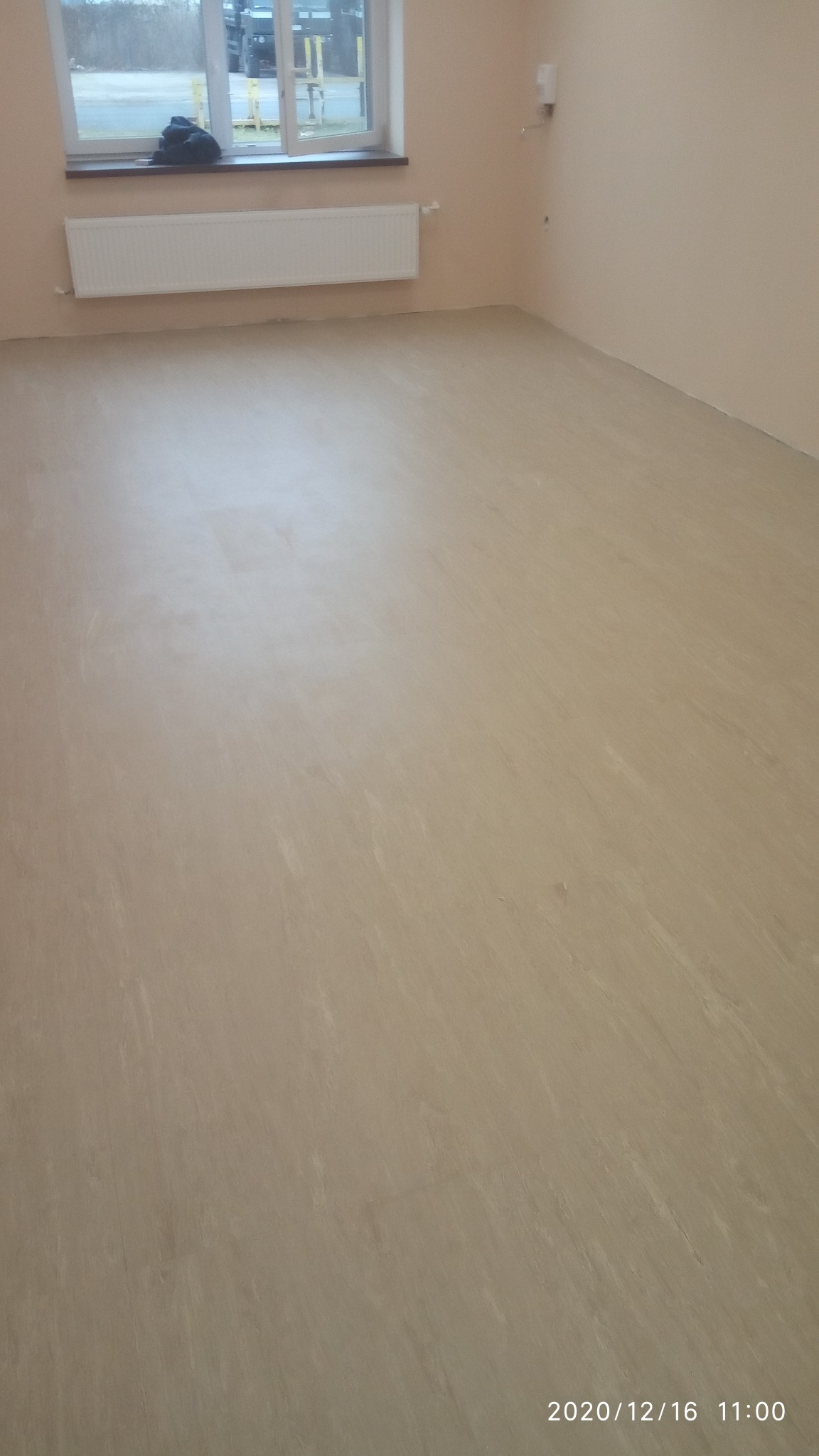 Wnętrze pokoju po wylaniu samopoziomującej wylewki podłogowej, widoczne ślady po wałku odpowietrzającym, okno z grzejnikiem i torba obok.