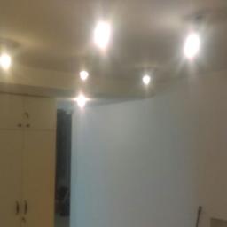 Bart-Tom-Dom - Wnętrze pokoju po odświeżeniu, z jasnymi ścianami, zabudową szaf w kolorze kremowym i nowoczesnym oświetleniem sufitowym.